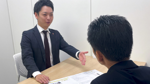 スーツを着た男性が机に広げた資料を元に対面の男性に向かって説明する様子